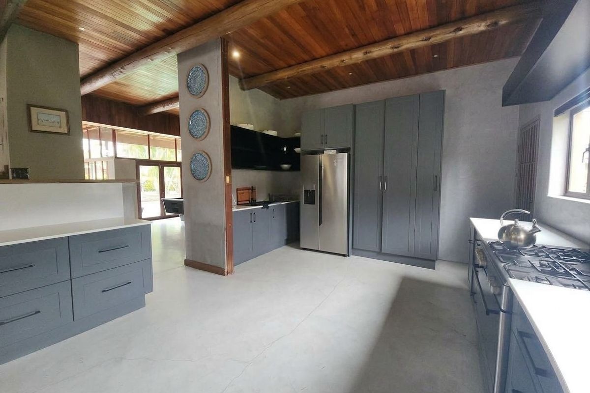 Modern kitchen featuring concrete floors, timber beam ceilings, dark grey cabinetry, stone countertops, and a gas cooktop with integrated appliances.