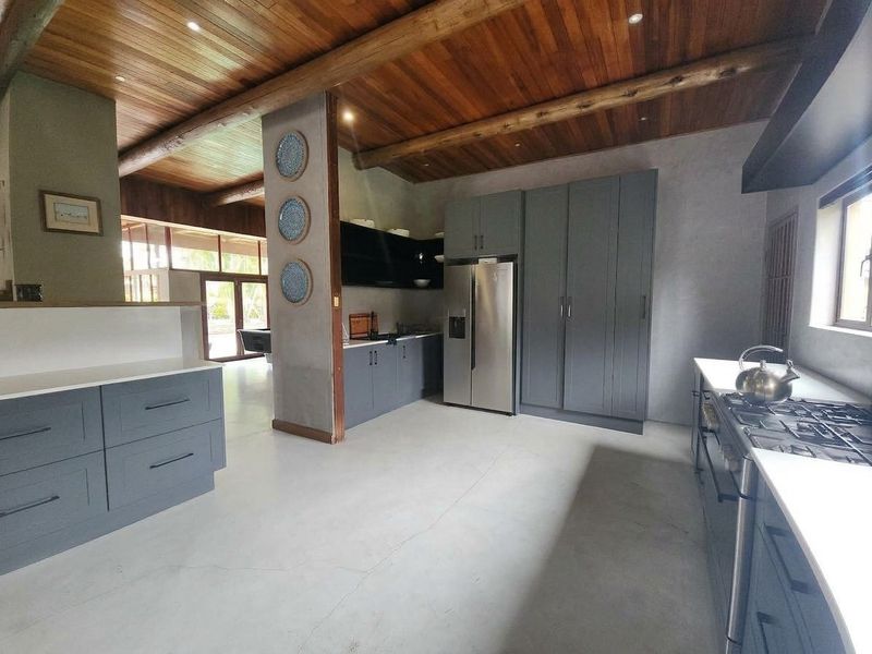 Modern kitchen featuring concrete floors, timber beam ceilings, dark grey cabinetry, stone countertops, and a gas cooktop with integrated appliances.