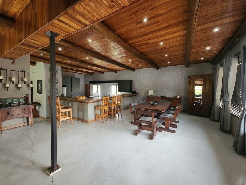 Spacious open-plan living and dining area featuring a high timber-clad ceiling, polished concrete floors, and a central kitchen island with breakfast bar seating.