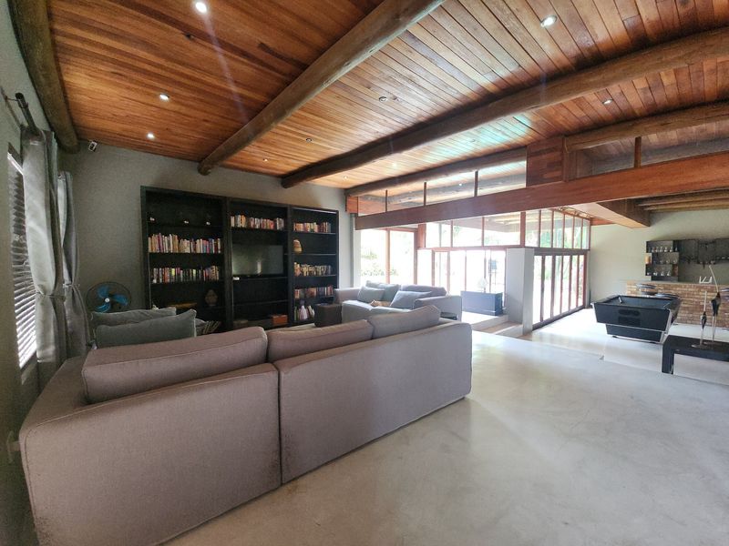 Spacious open-plan living area featuring a striking exposed timber beam ceiling, polished concrete floors, and large glass doors providing ample natural light.