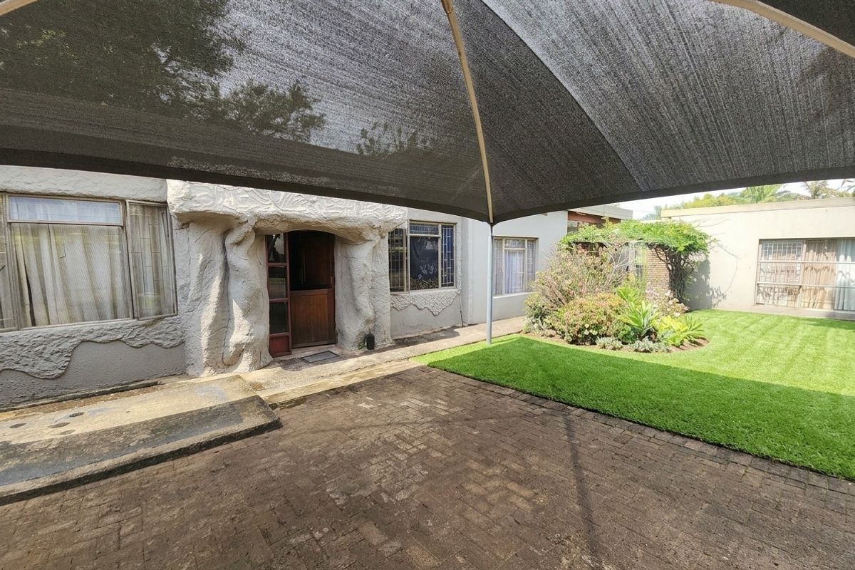 Rear exterior view featuring a paved patio area, a large shade sail, a well-maintained lawn, and a unique decorative stone entrance feature.