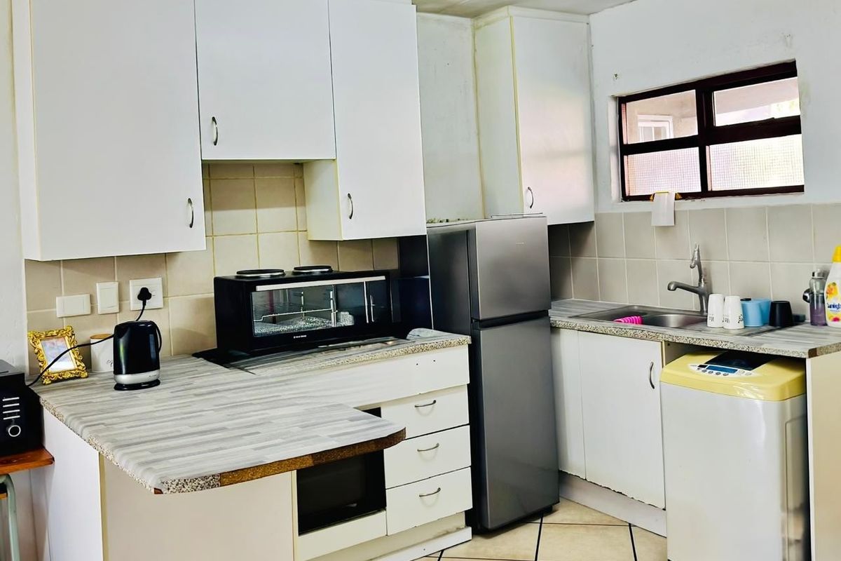 A compact kitchen featuring white cabinetry, laminate countertops, tiled backsplash, and tiled flooring, providing a functional workspace with integrated sink and storage.