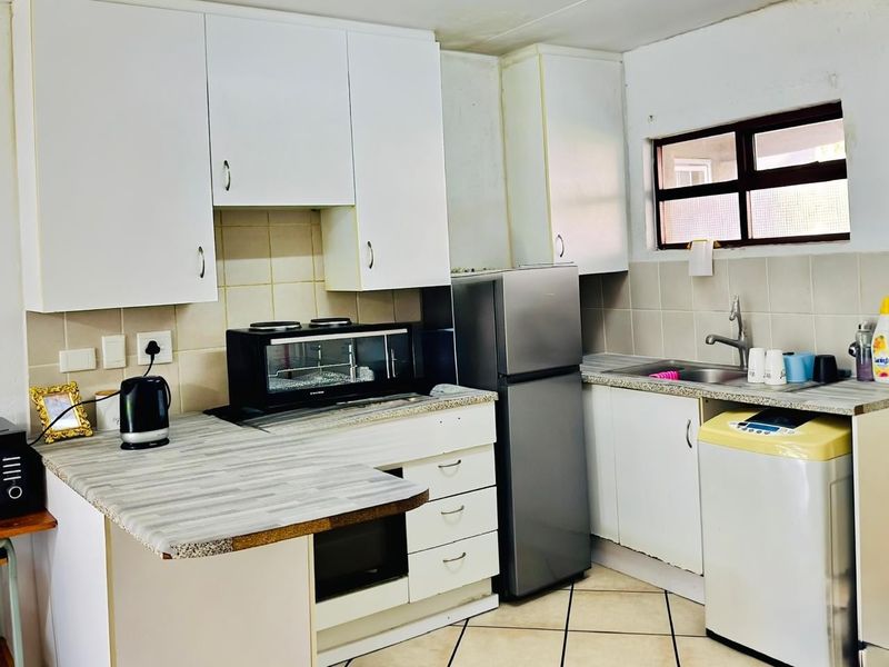 A compact kitchen featuring white cabinetry, laminate countertops, tiled backsplash, and tiled flooring, providing a functional workspace with integrated sink and storage.