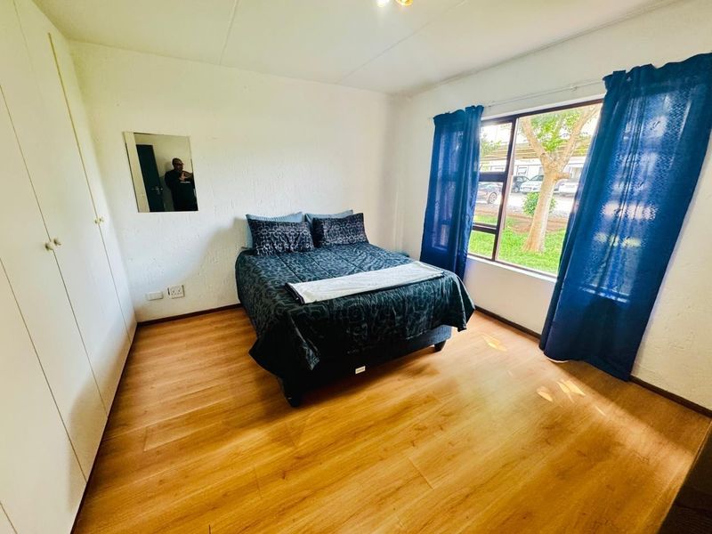 A well-lit bedroom featuring laminate flooring, built-in cupboards, and a large window providing natural light and exterior views.