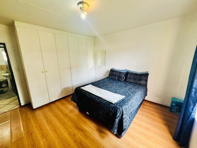 A bedroom featuring laminate flooring, built-in cupboards, and a ceiling light fixture, with an adjacent view into a bathroom.