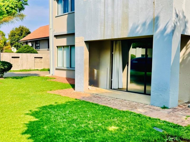Rear view of the apartment building featuring a paved patio area, sliding glass doors, and a well-maintained lawn.