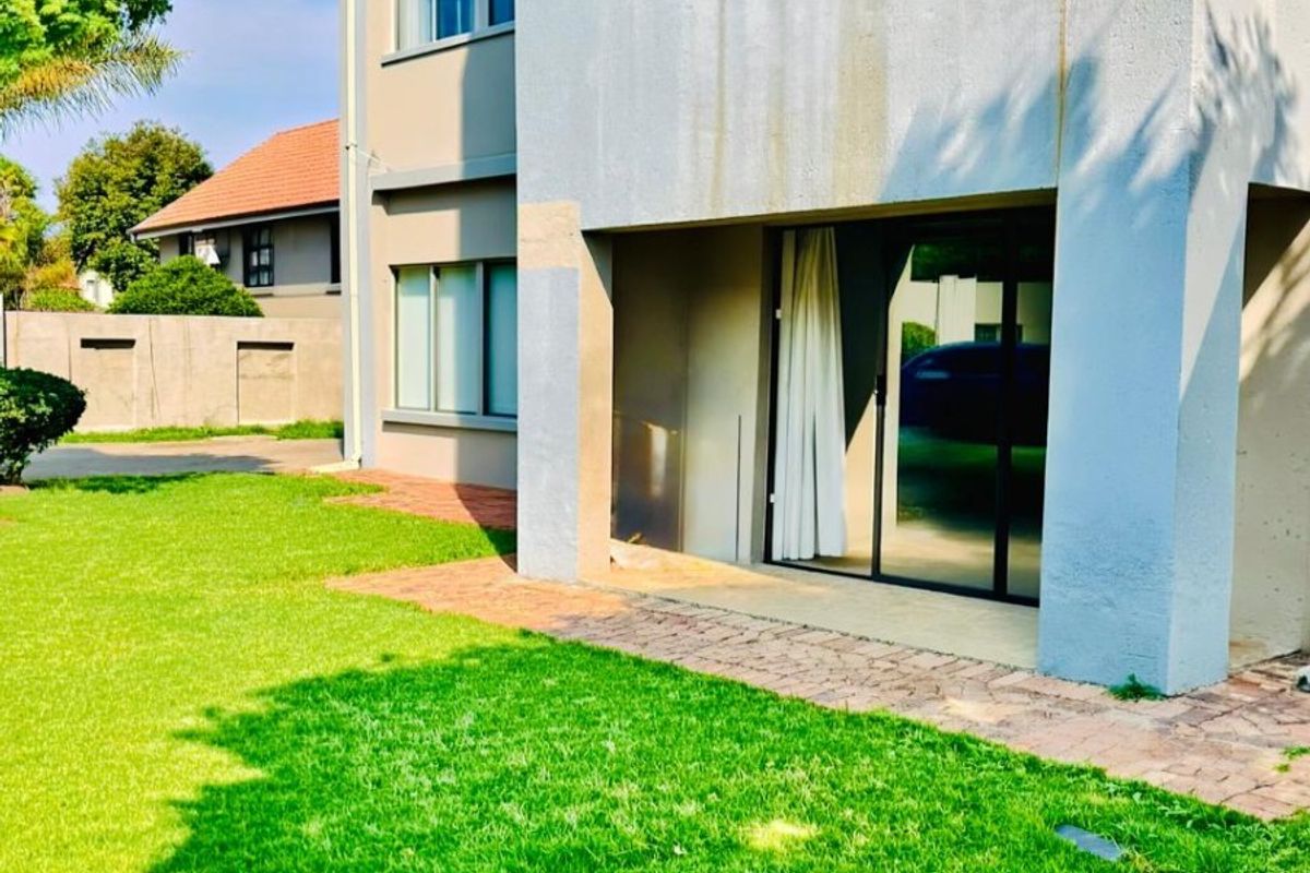 Rear view of the apartment building featuring a paved patio area, sliding glass doors, and a well-maintained lawn.