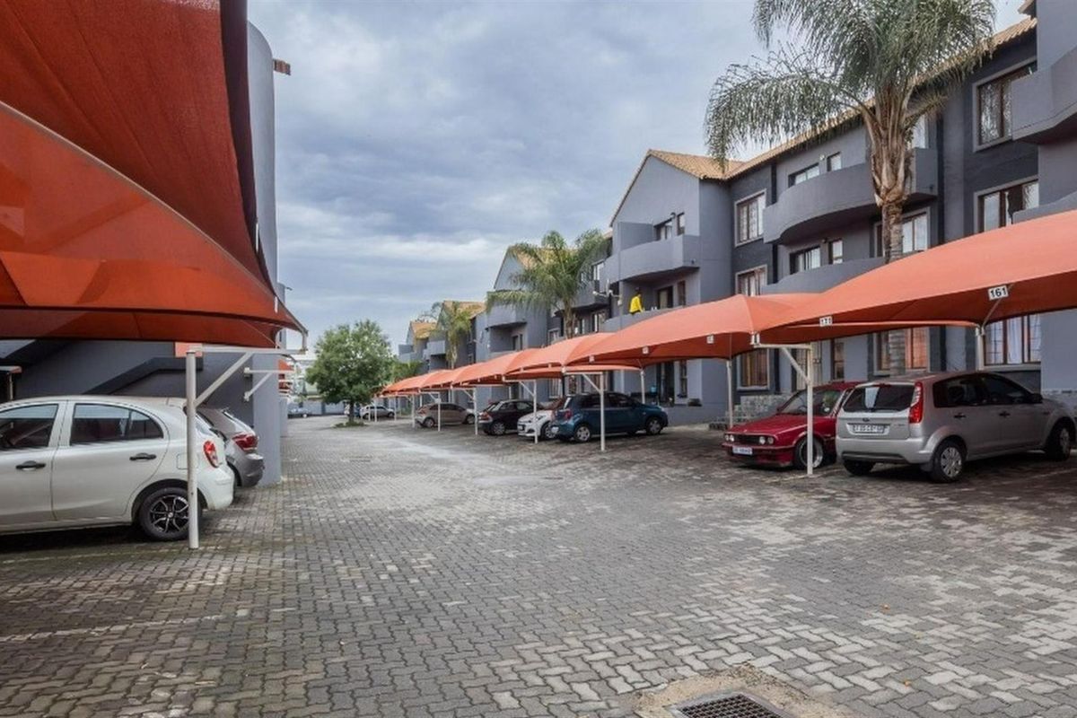 Exterior view of an apartment complex featuring a paved parking area with dedicated shade cloth carports for residents.