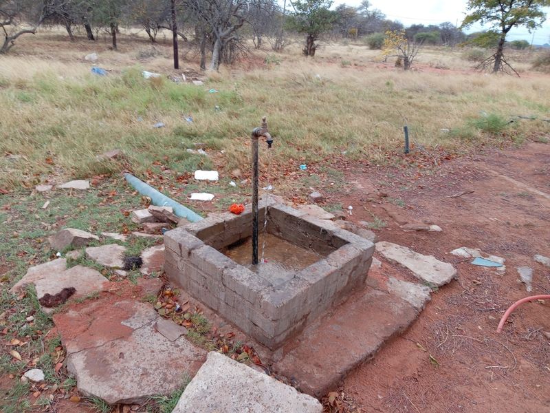 An outdoor utility water point featuring a masonry basin and a metal tap, situated in a rural farm landscape.