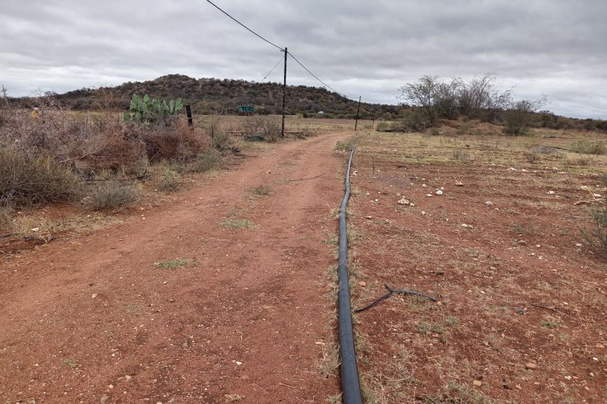 An expansive view of the farm landscape featuring an unpaved access track, overhead utility lines, and exposed irrigation infrastructure running across the terrain.