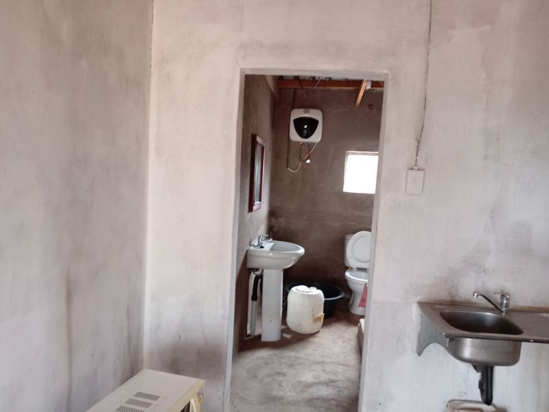 A basic bathroom and utility area featuring a pedestal basin, toilet, and electric water heater with unfinished wall surfaces.