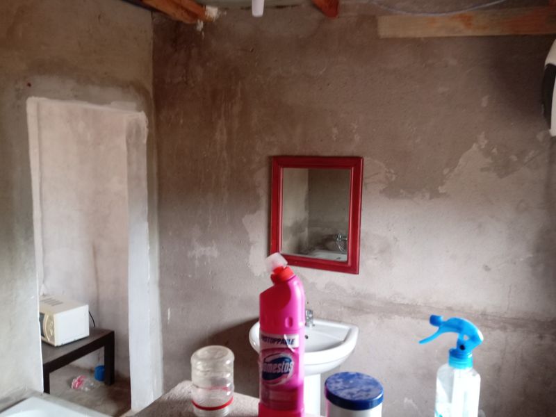 A basic bathroom featuring a pedestal basin and wall mirror, currently in an unfinished state with exposed plaster walls and ceiling.