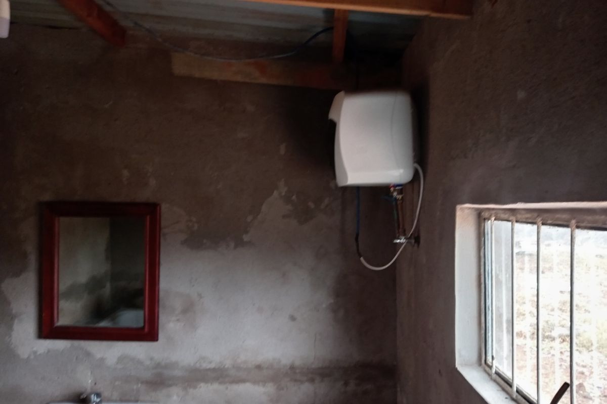 A basic bathroom space featuring raw concrete walls, a wall-mounted water heater, and a basin, requiring significant finishing and renovation.
