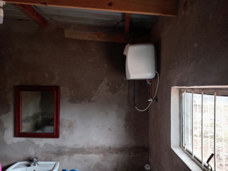 A basic bathroom space featuring raw concrete walls, a wall-mounted water heater, and a basin, requiring significant finishing and renovation.