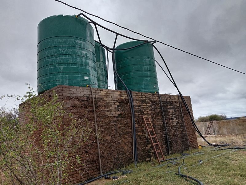 Outdoor water storage infrastructure featuring multiple large green tanks mounted on a raised brick masonry platform with connected plumbing systems.
