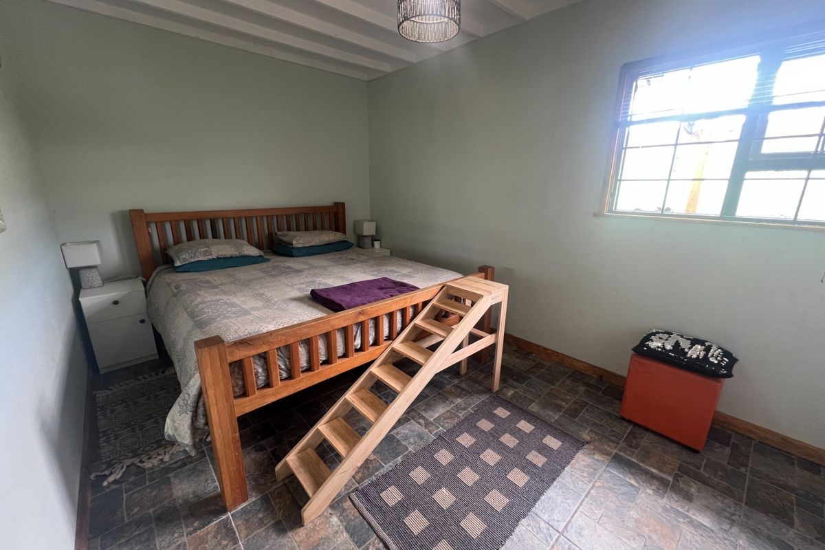 A bedroom featuring tiled flooring, exposed beam ceiling, and a grid-pattern window, providing a functional space with a rustic aesthetic.