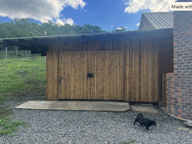 A rustic timber-clad garage featuring sliding barn-style doors, a metal roof, and a brick chimney, set against a rural landscape.