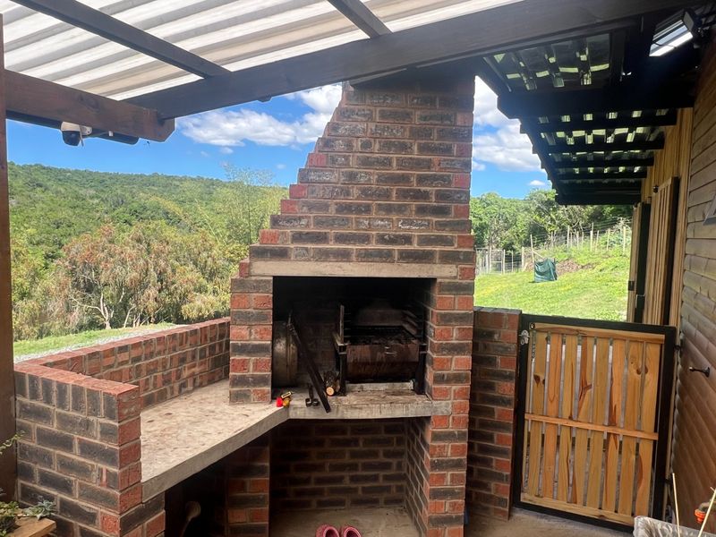 Covered outdoor patio area featuring a built-in brick braai with concrete prep space, overlooking the surrounding farm landscape.