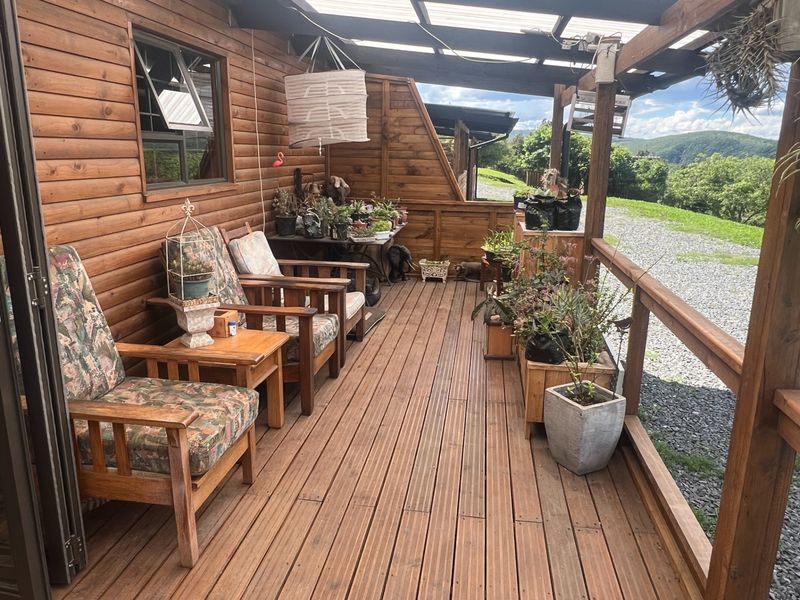 A covered timber patio featuring wooden decking, wall cladding, and a balustrade, offering an elevated outdoor space with scenic landscape views.
