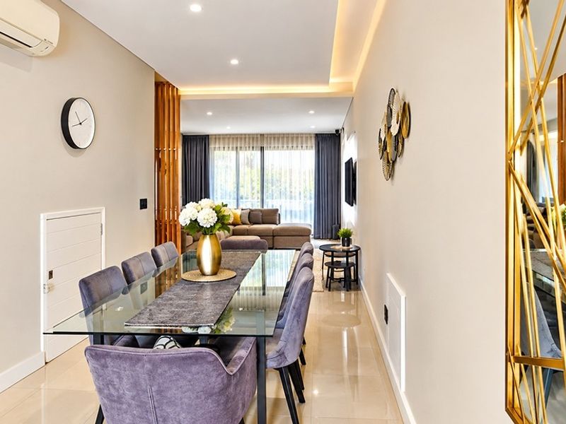 A modern, well-lit dining area featuring sleek tiled flooring, recessed ceiling lighting with cove accents, and a timber slat feature divider.