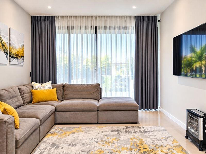 A modern, well-maintained living room featuring recessed lighting, a large sliding glass door with floor-to-ceiling curtains, and wall-mounted television connectivity.