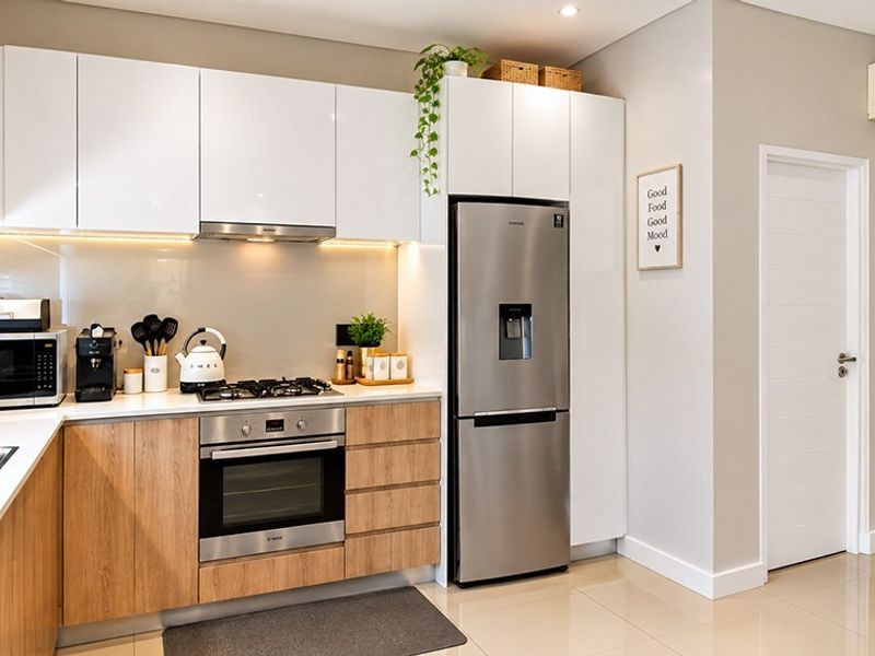Modern kitchen featuring sleek white upper cabinets, wood-finish lower cabinetry, integrated appliances, gas hob, and polished tiled flooring.