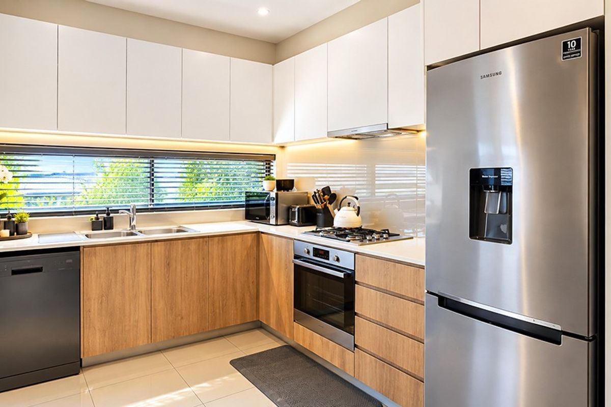 Modern kitchen featuring sleek white and wood-grain cabinetry, stone benchtops, integrated appliances, and high-quality finishes with ample natural light.