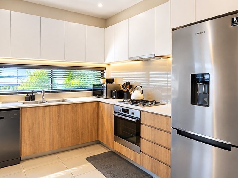 Modern kitchen featuring sleek white and wood-grain cabinetry, stone benchtops, integrated appliances, and high-quality finishes with ample natural light.