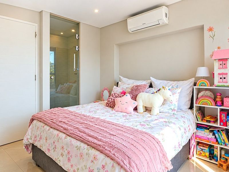 A well-maintained bedroom featuring tiled flooring, recessed lighting, and a wall-mounted air conditioning unit, with an adjacent glass-paneled door.