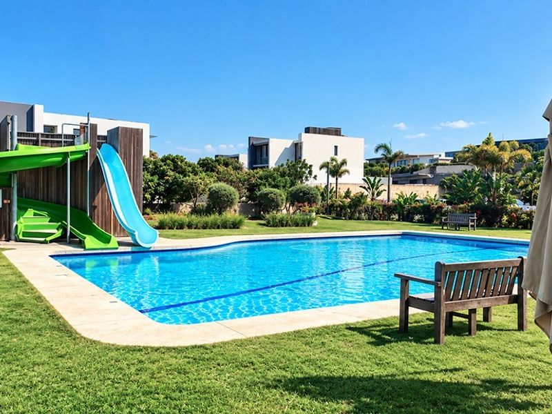 A well-maintained outdoor swimming pool area featuring a built-in slide, timber-clad structure, and surrounding landscaped garden space.