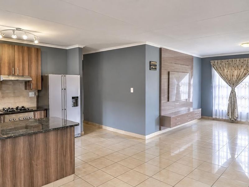 Spacious open-plan living area featuring a modern kitchen with granite countertops, gas hob, and a built-in media unit, finished with neutral tiled flooring.