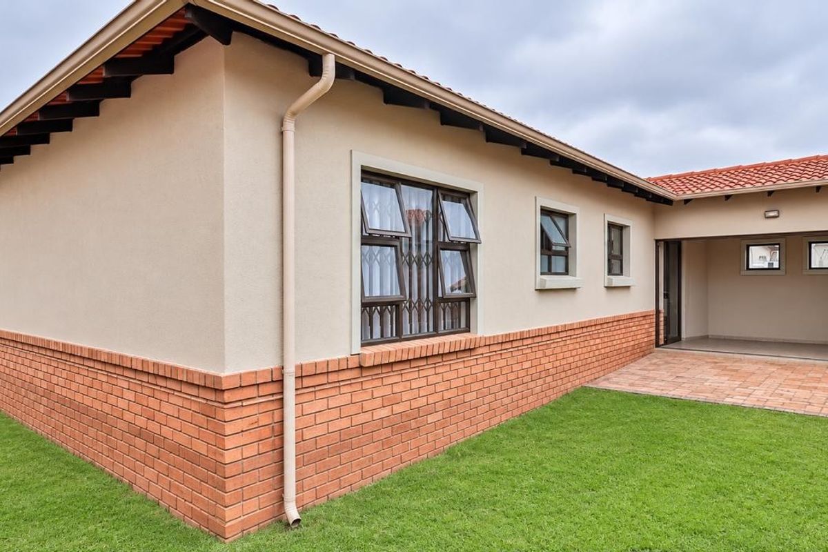 Rear view of the house featuring a brick plinth, terracotta tiled roof, casement windows with security bars, and a paved patio area leading to the lawn.