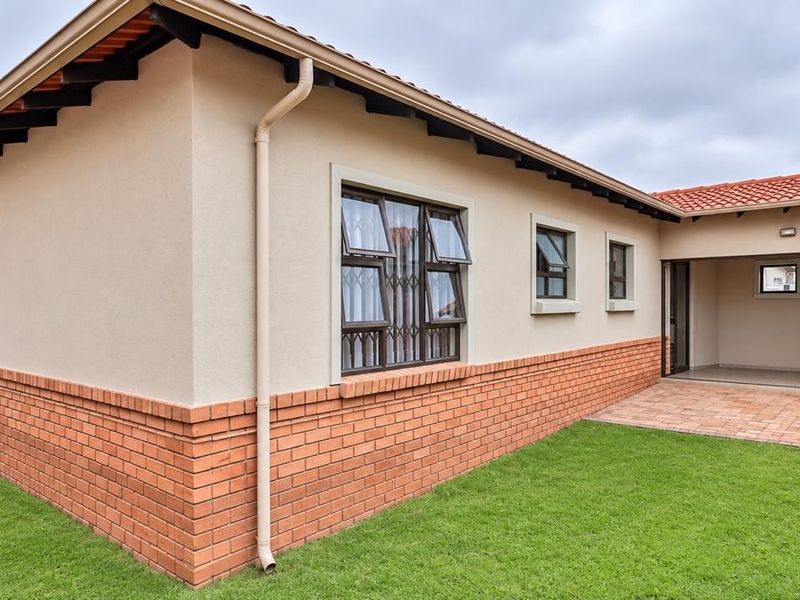 Rear view of the house featuring a brick plinth, terracotta tiled roof, casement windows with security bars, and a paved patio area leading to the lawn.