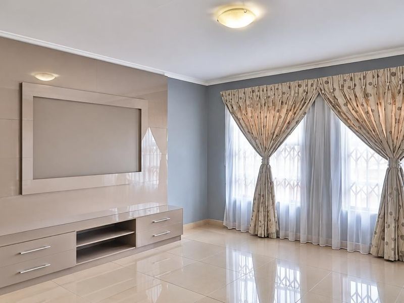 Spacious living room featuring polished porcelain floor tiles, a modern built-in media unit, and large windows with security gates.