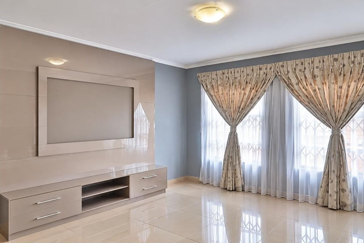 Spacious living room featuring polished porcelain floor tiles, a modern built-in media unit, and large windows with security gates.