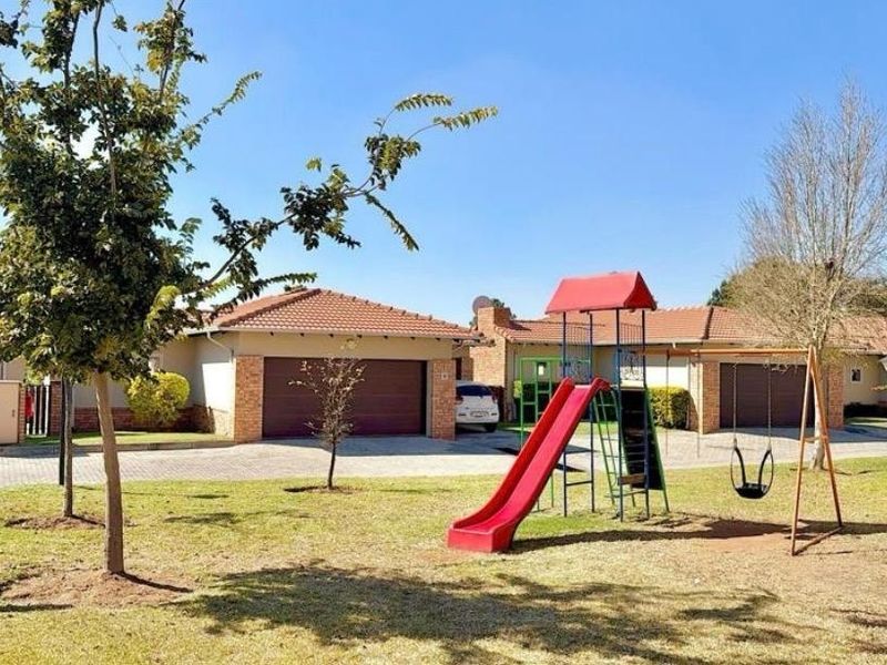A well-maintained communal garden area featuring a children's playground, paved driveways, and residential garage access.