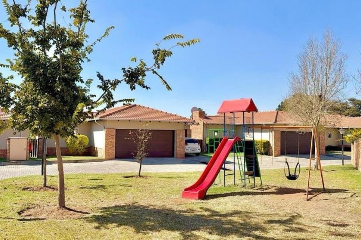 A well-maintained communal garden area featuring a children's playground, paved driveways, and residential garage access.