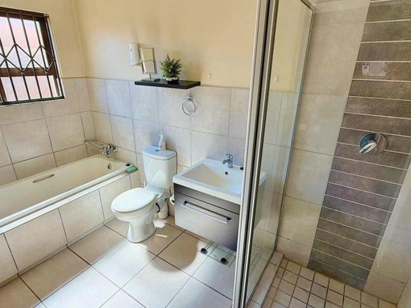 A functional bathroom featuring a bathtub, separate shower enclosure, vanity unit, and toilet with neutral wall and floor tiling.