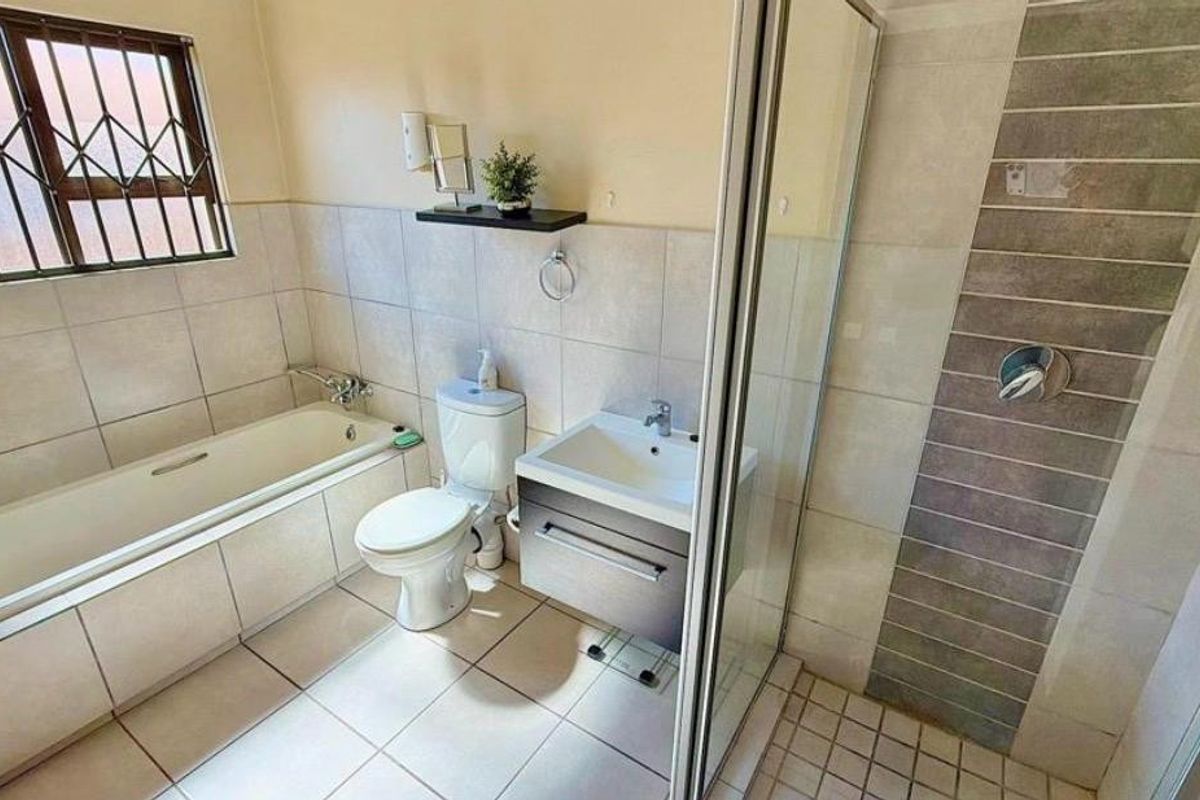 A functional bathroom featuring a bathtub, separate shower enclosure, vanity unit, and toilet with neutral wall and floor tiling.