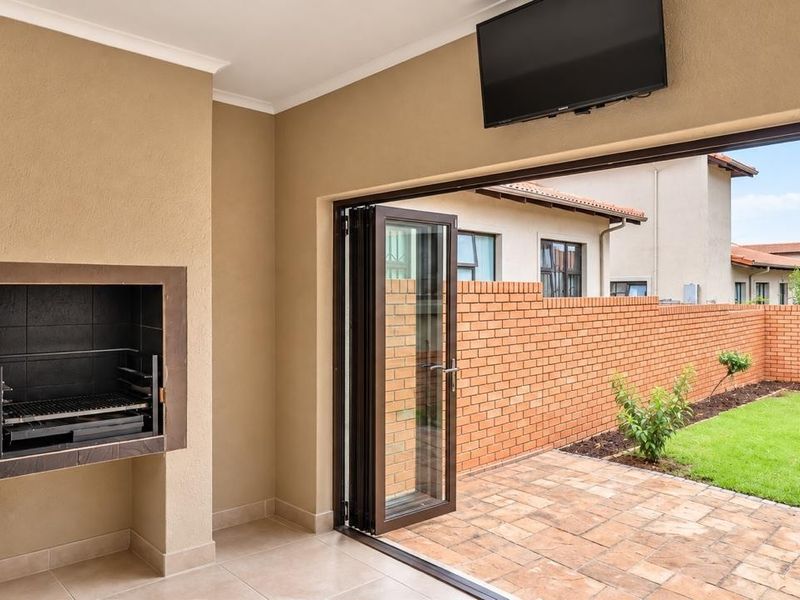 Covered patio featuring a built-in braai and bi-fold doors opening onto a private garden with a brick boundary wall.