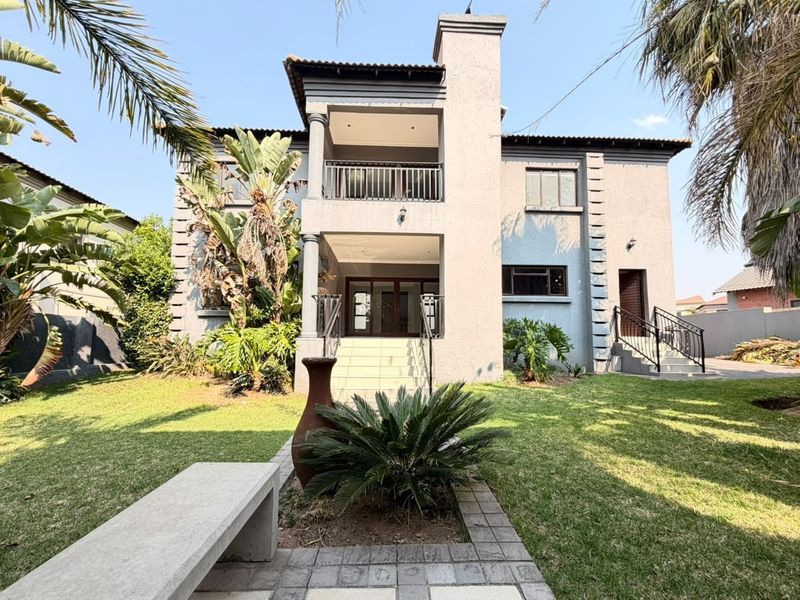 Rear view of a double-story house featuring a balcony, chimney, and a landscaped garden with a paved walkway and concrete bench.