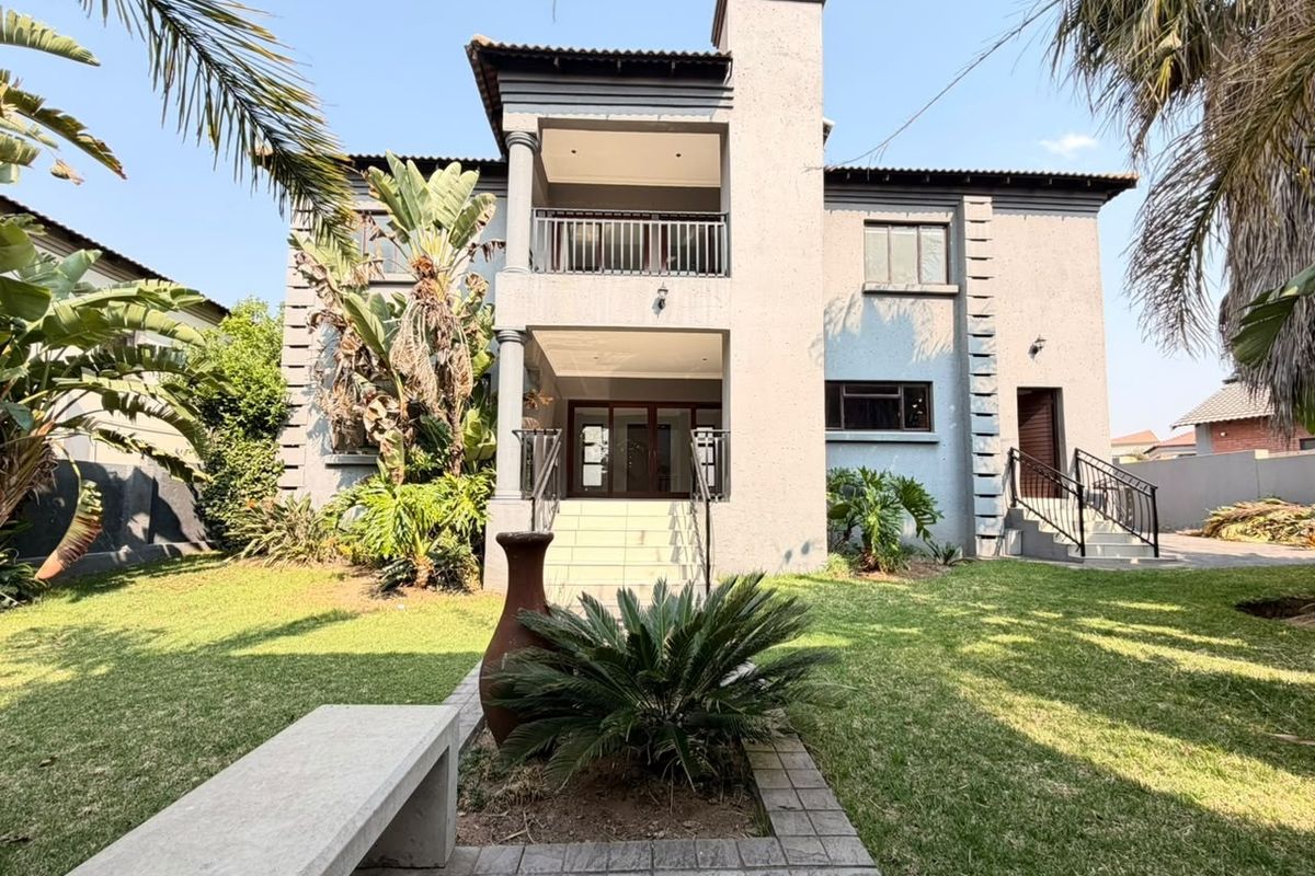 Rear view of a double-story house featuring a balcony, chimney, and a landscaped garden with a paved walkway and concrete bench.