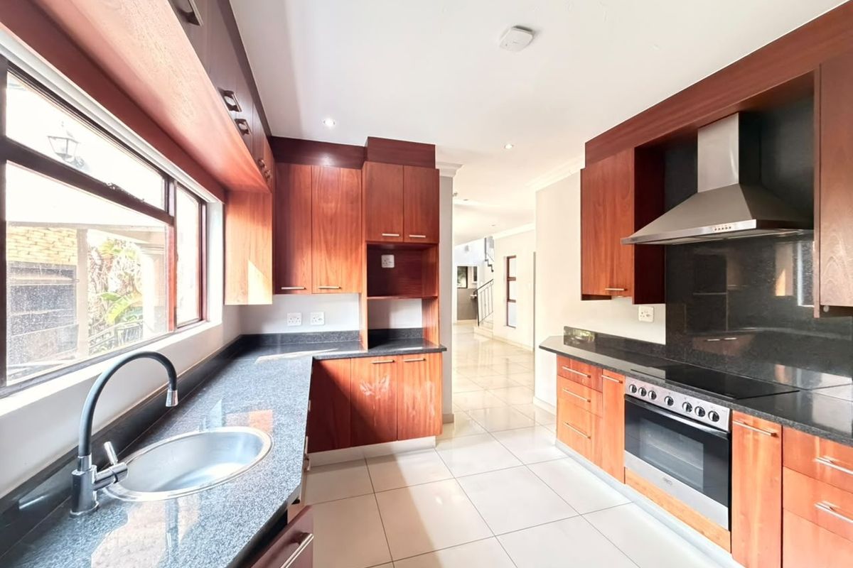 A modern kitchen featuring dark granite countertops, rich wooden cabinetry, stainless steel appliances, and neutral ceramic floor tiles in a bright, open layout.