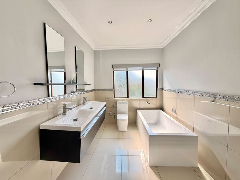 A modern, well-maintained bathroom featuring a sleek double vanity, a clean built-in bathtub, and neutral tiling throughout.