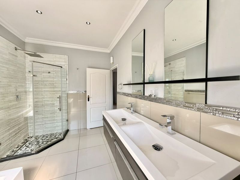 Modern bathroom featuring a double vanity with sleek basins, a glass-enclosed shower with mosaic tile accents, and contemporary wall-mounted mirrors.
