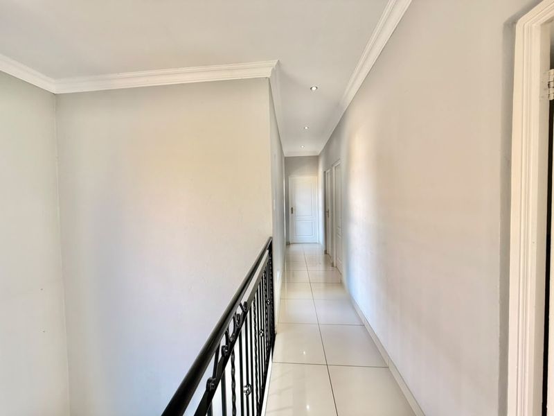 A bright and spacious hallway featuring tiled flooring, recessed downlighting, and a decorative wrought iron balustrade overlooking the lower level.