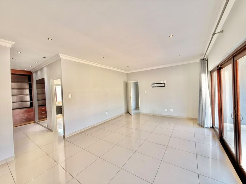 Spacious, light-filled living area featuring neutral tiled flooring, recessed downlighting, built-in wooden cabinetry, and large sliding glass doors leading to the exterior.