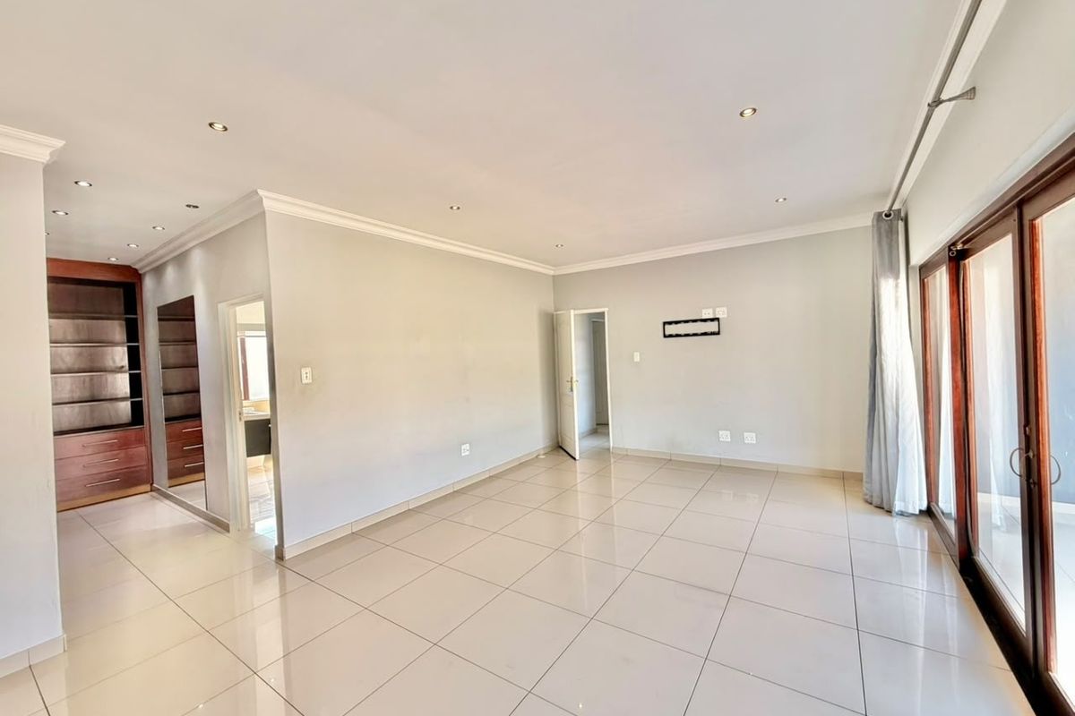 Spacious, light-filled living area featuring neutral tiled flooring, recessed downlighting, built-in wooden cabinetry, and large sliding glass doors leading to the exterior.