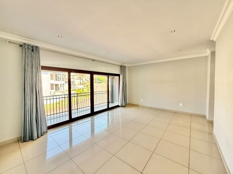 A bright and spacious living area featuring neutral tiled flooring, recessed downlights, and large sliding glass doors that open onto a balcony.