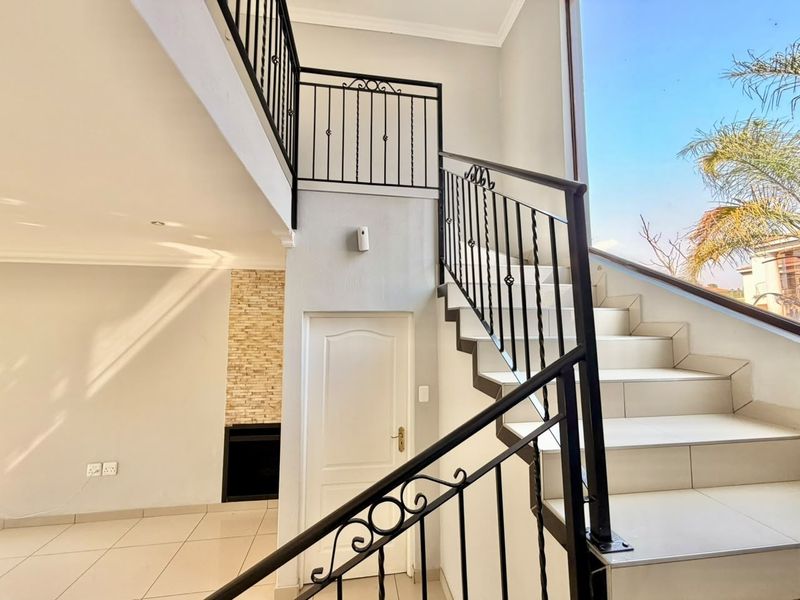 Bright hallway featuring a tiled staircase with wrought iron balustrades, leading to an open area with a stone-clad fireplace feature.